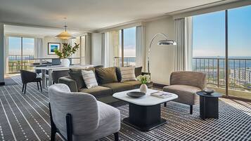 A modern hotel room with a balcony, a sofa, a coffee table, and a dining area.