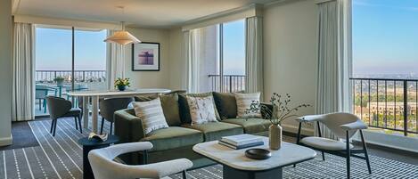 A modern hotel room with a large balcony, a sofa set, a dining table, and a patterned floor.