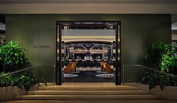 A modern bar area with a circular bar counter, surrounded by orange chairs and a round table. at Pendry Newport Beach