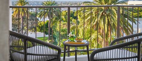 A balcony with wicker chairs and a small table with a flower vase and fruit bowl.