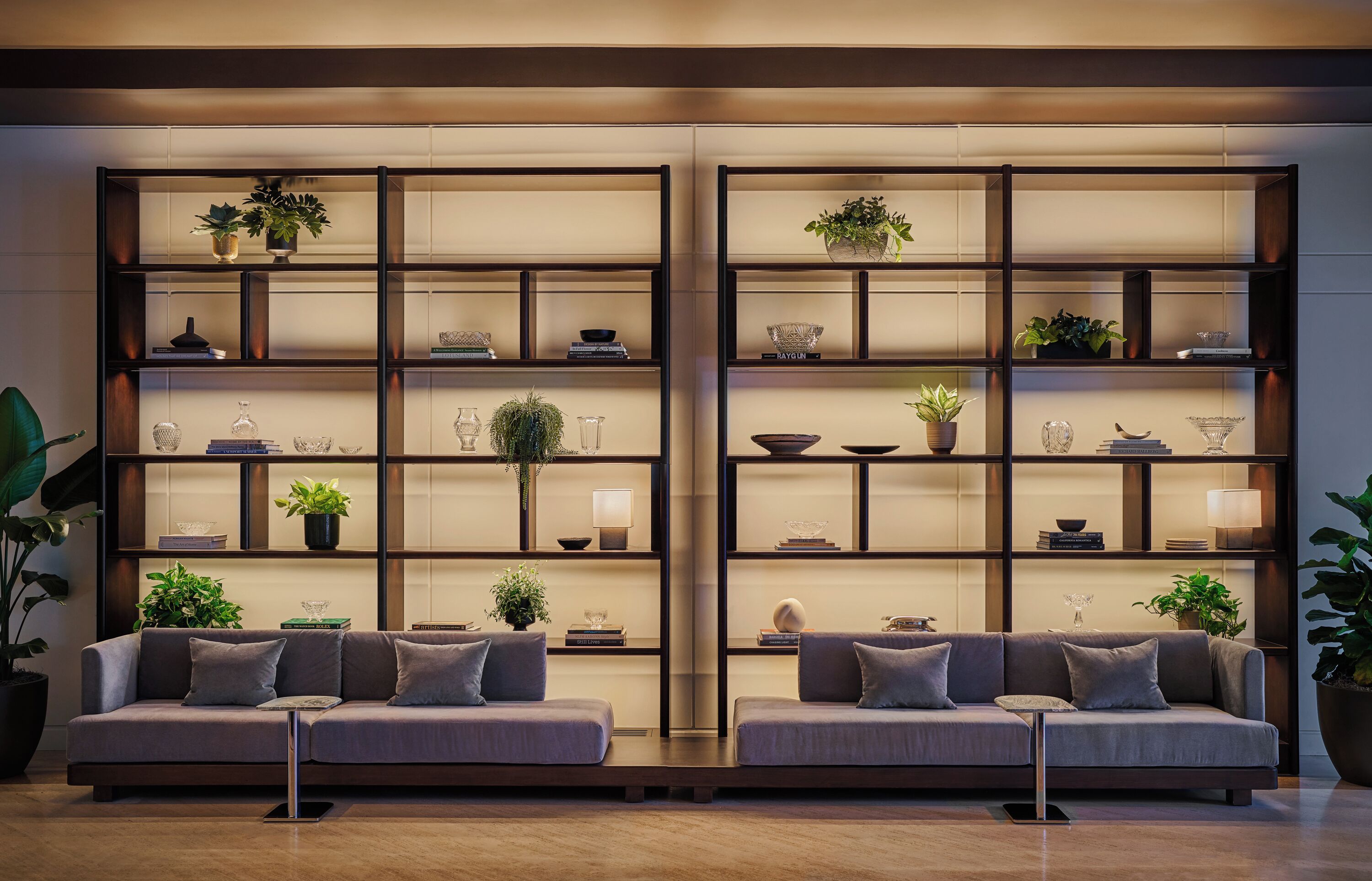 A modern living room with two sofas, a coffee table, and a large bookshelf with decorative items and plants.