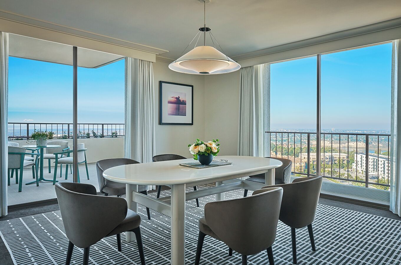A modern hotel room with a balcony, a round dining table, and a view of the cityscape.