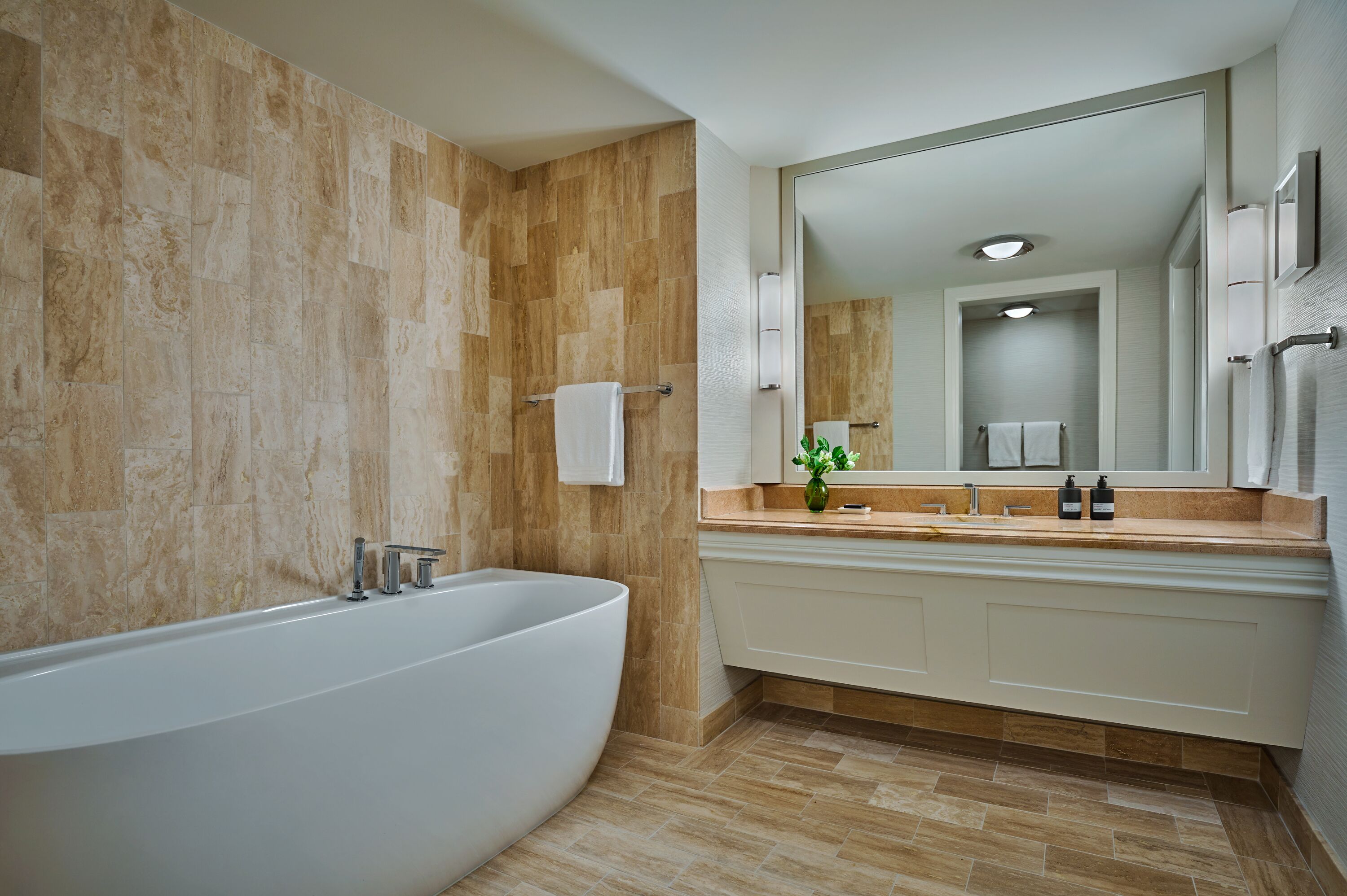 Un baño moderno con una bañera independiente, un espejo grande y un tocador con lavamanos y toallero.
