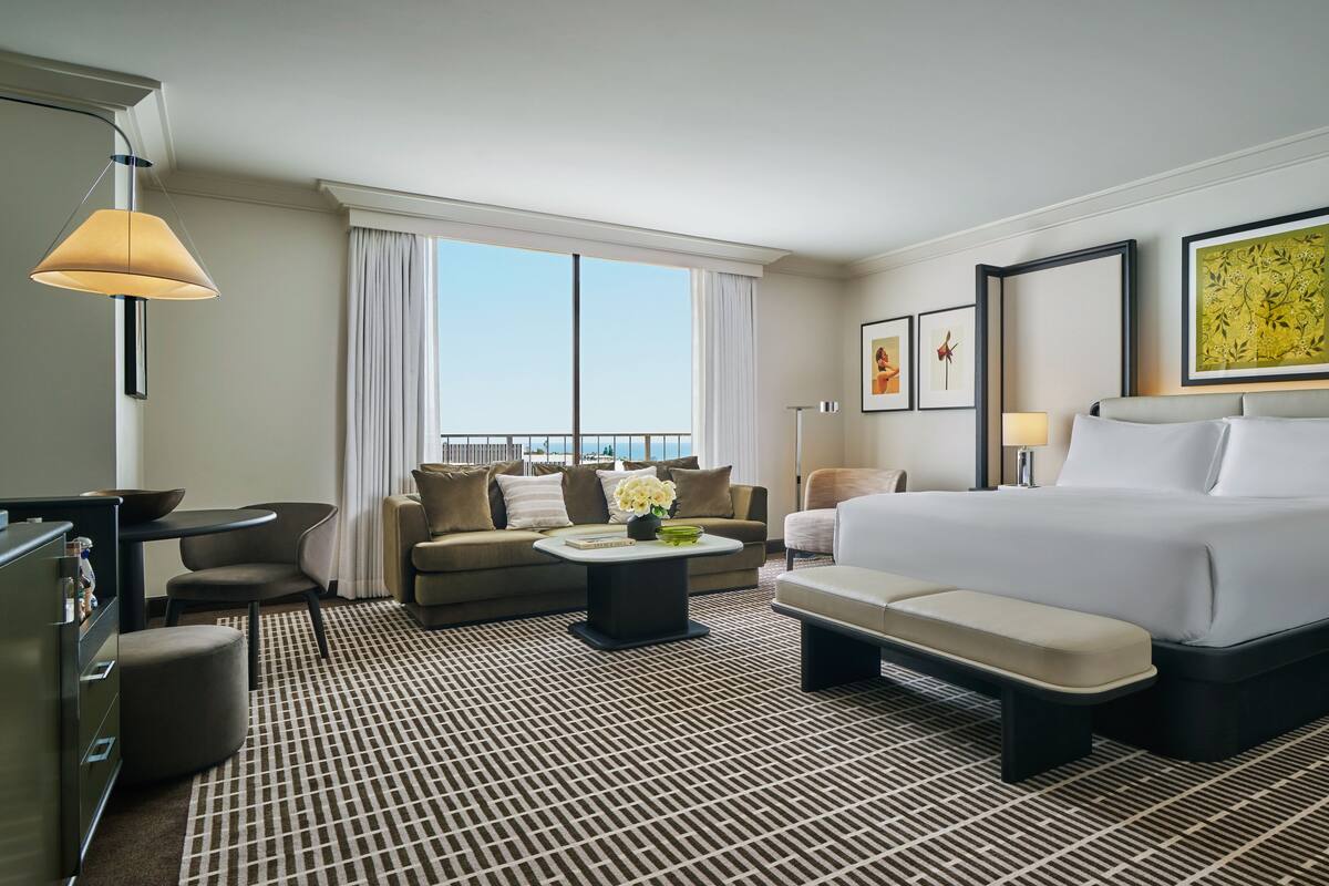 A hotel room with a large bed, a sofa, a small table, a desk, and a view of the outdoors.