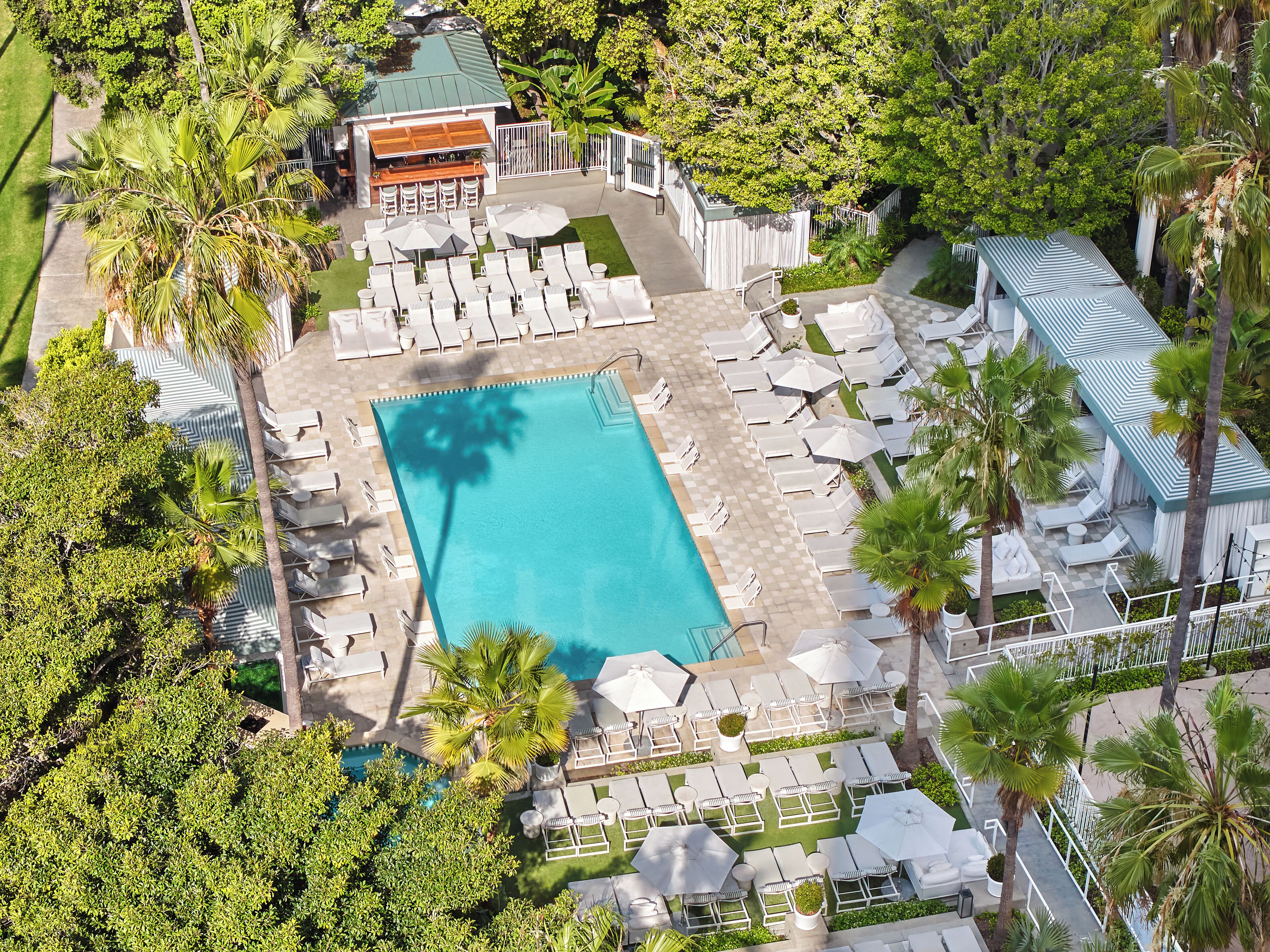 Ett flygbildsfoto av ett semesterområde med en swimmingpool, solstolar och en bar, omgivet av palmer.