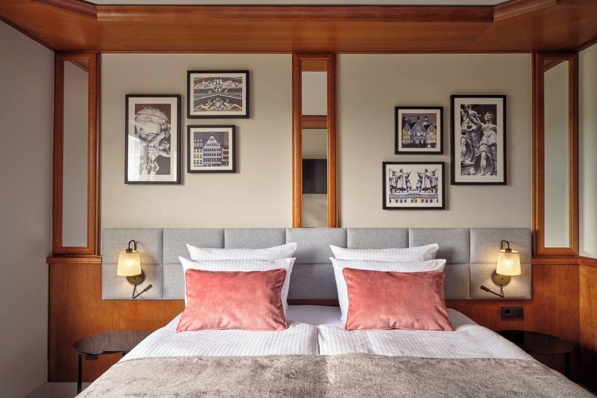 Habitación de hotel con una cama grande, dos mesitas de noche, un espejo y cuadros en la pared.