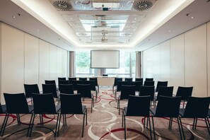 A conference room with rows of chairs, a large screen, and a patterned carpet. - Leonardo Frankfurt City South (Frankfurt)