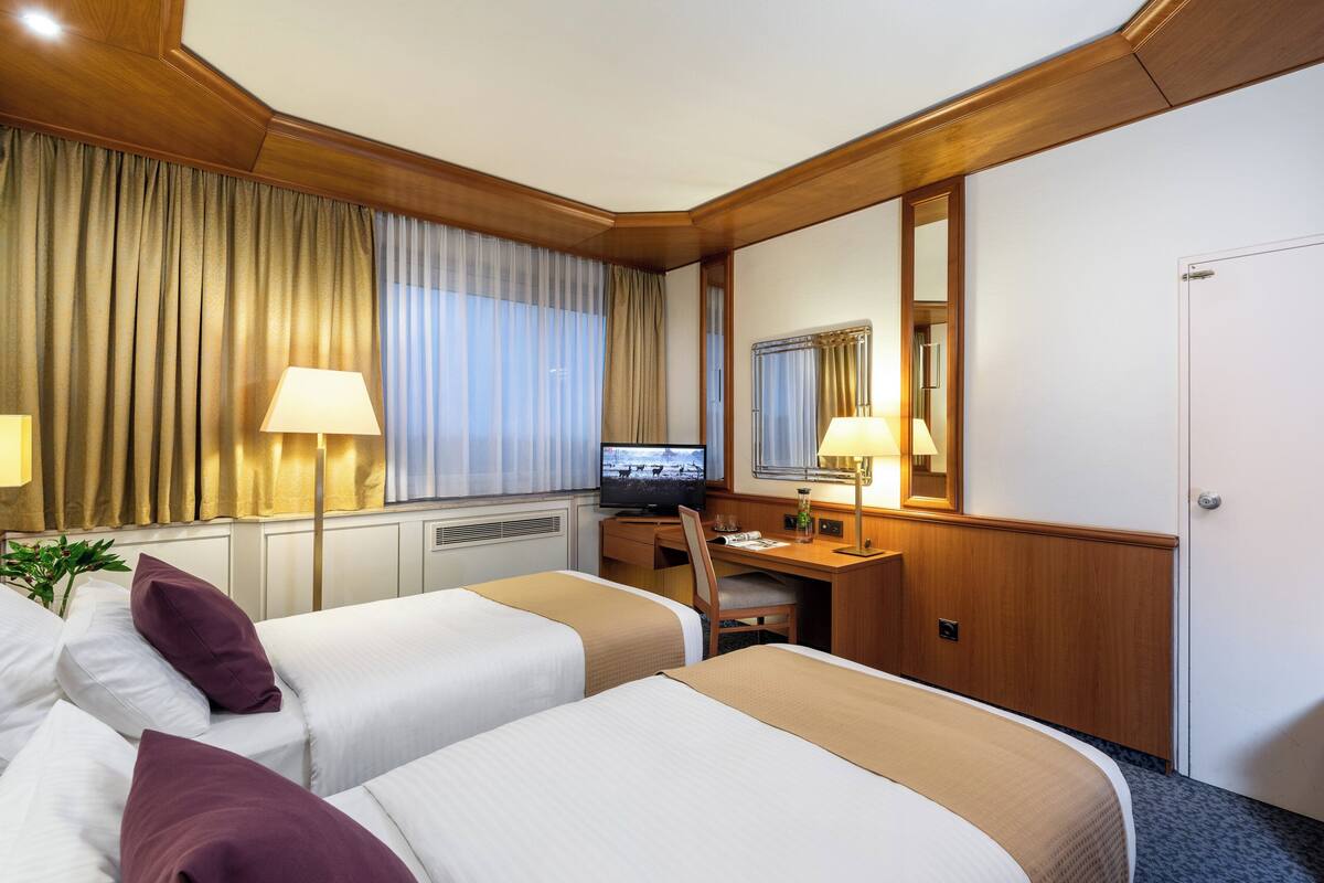 Habitación de hotel con dos camas, un escritorio con computadora, una silla y un espejo grande.