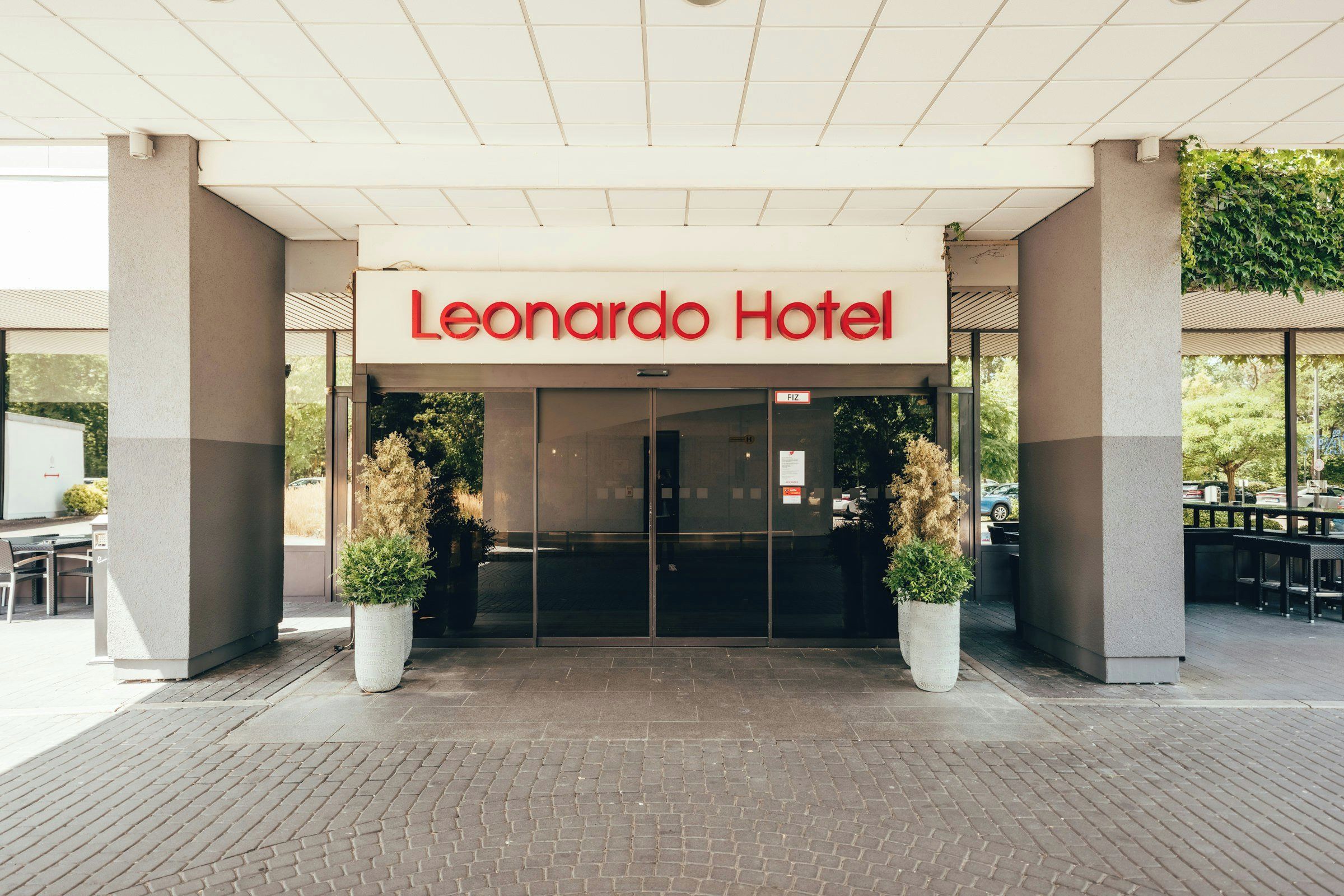 L'entrée de l'hôtel Leonard est clairement indiquée par un panneau, agrémentée de deux plantes en pot et d'une zone pavée de briques.