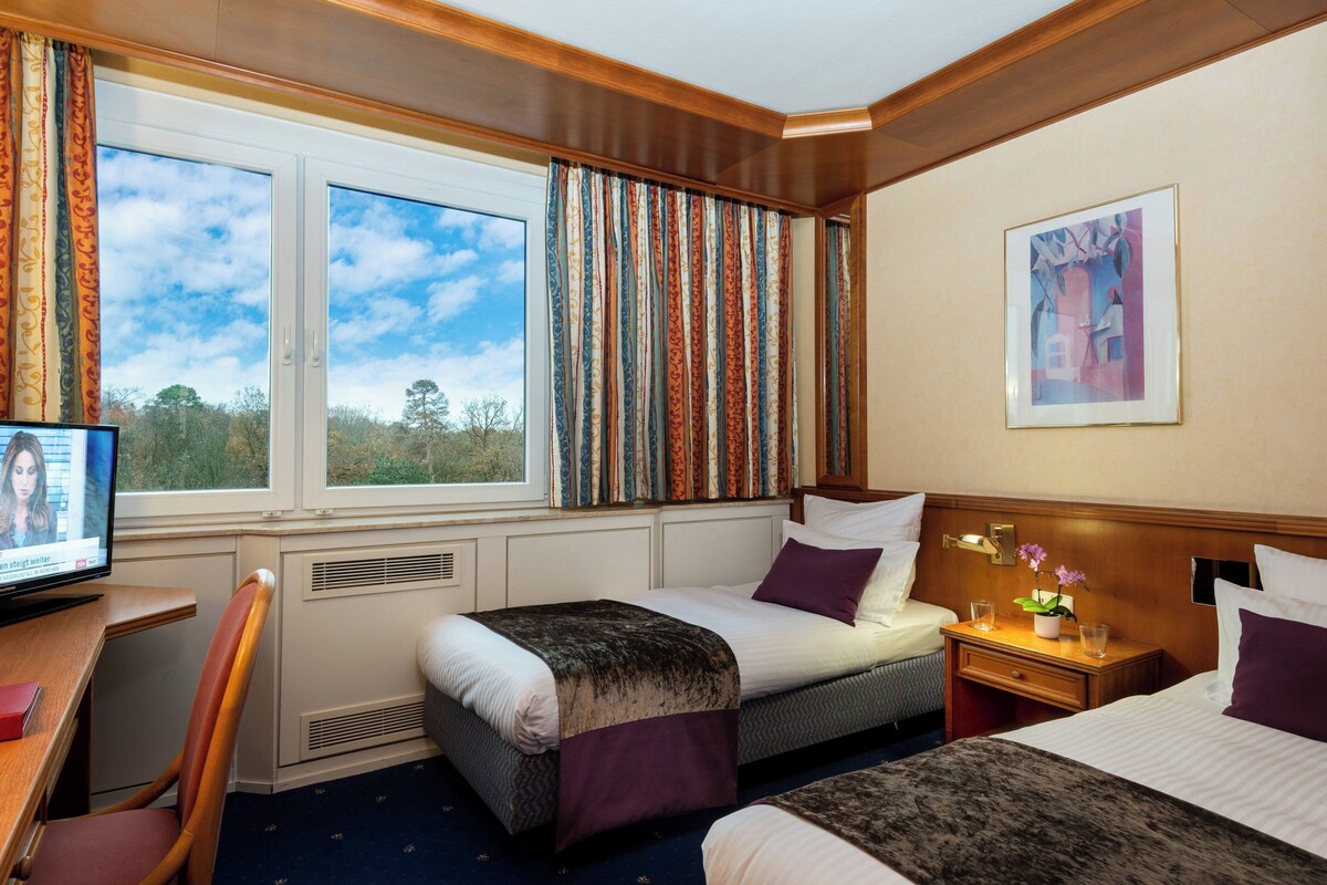A hotel room with two beds, a desk with a computer, a chair, and a window with curtains.