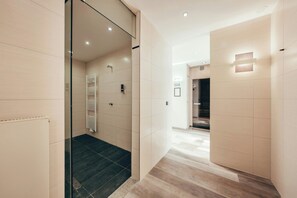 A modern hotel hallway with a glass door leading to a shower area, a wooden floor, and a wall-mounted light fixture. - Leonardo Frankfurt City South (Frankfurt)