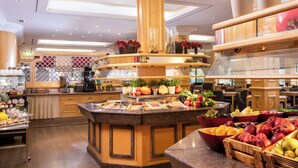 Un vestíbulo de hotel amplio y bien iluminado, con una isla central que ofrece frutas, verduras, una cafetera y plantas decorativas.