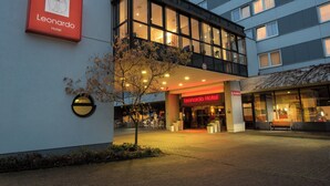 Entrada de hotel con diseño moderno, destacada por un letrero llamativo y un espacio al aire libre con mobiliario para recibir a los huéspedes.