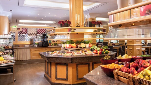 Un vestíbulo de hotel amplio y bien iluminado, con una isla central que ofrece frutas, verduras, una cafetera y plantas decorativas.
