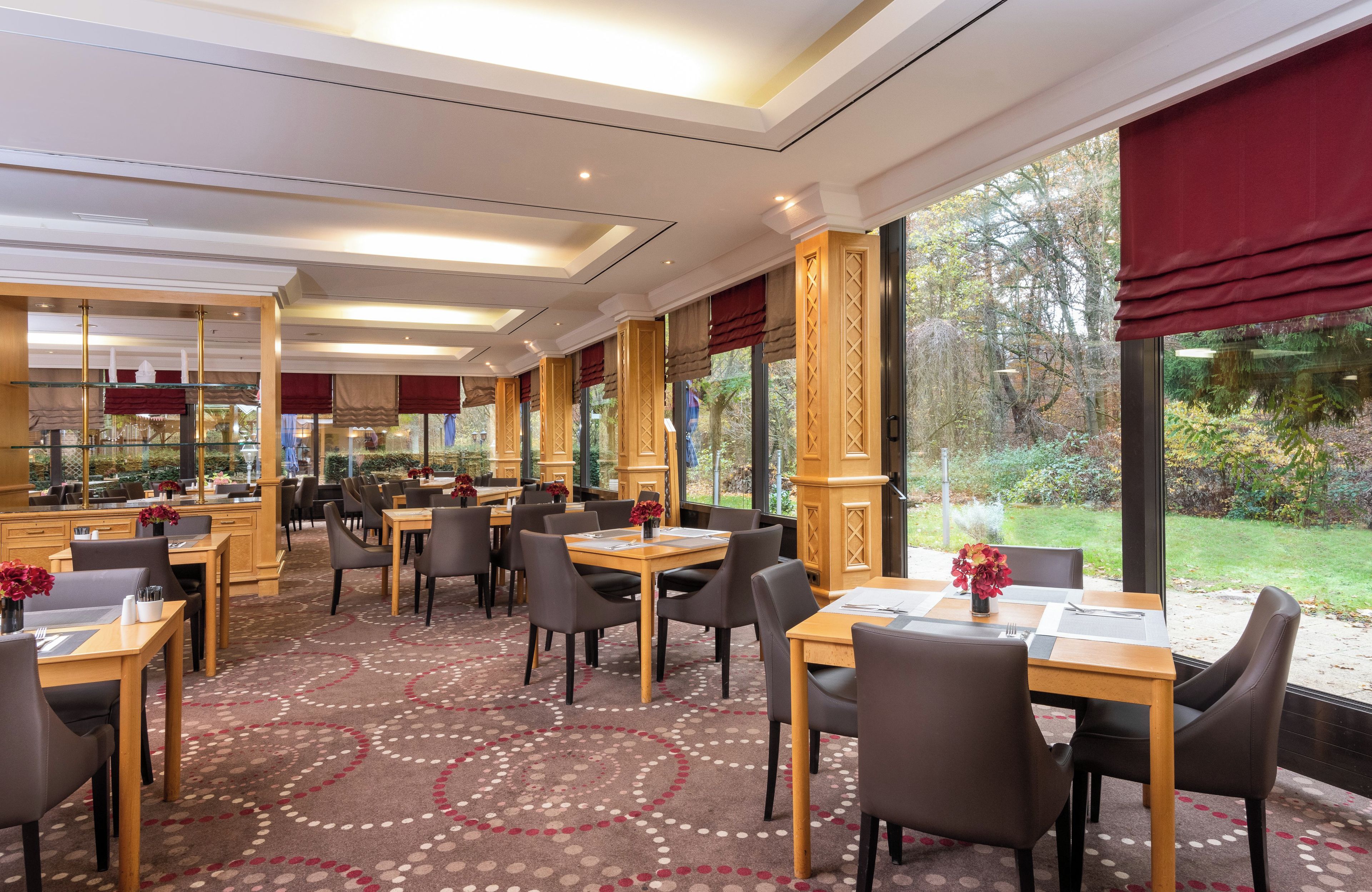 Ein Speisebereich eines Hotels mit Tischen, Stühlen, großen Fenstern und einem gemusterten Teppich.