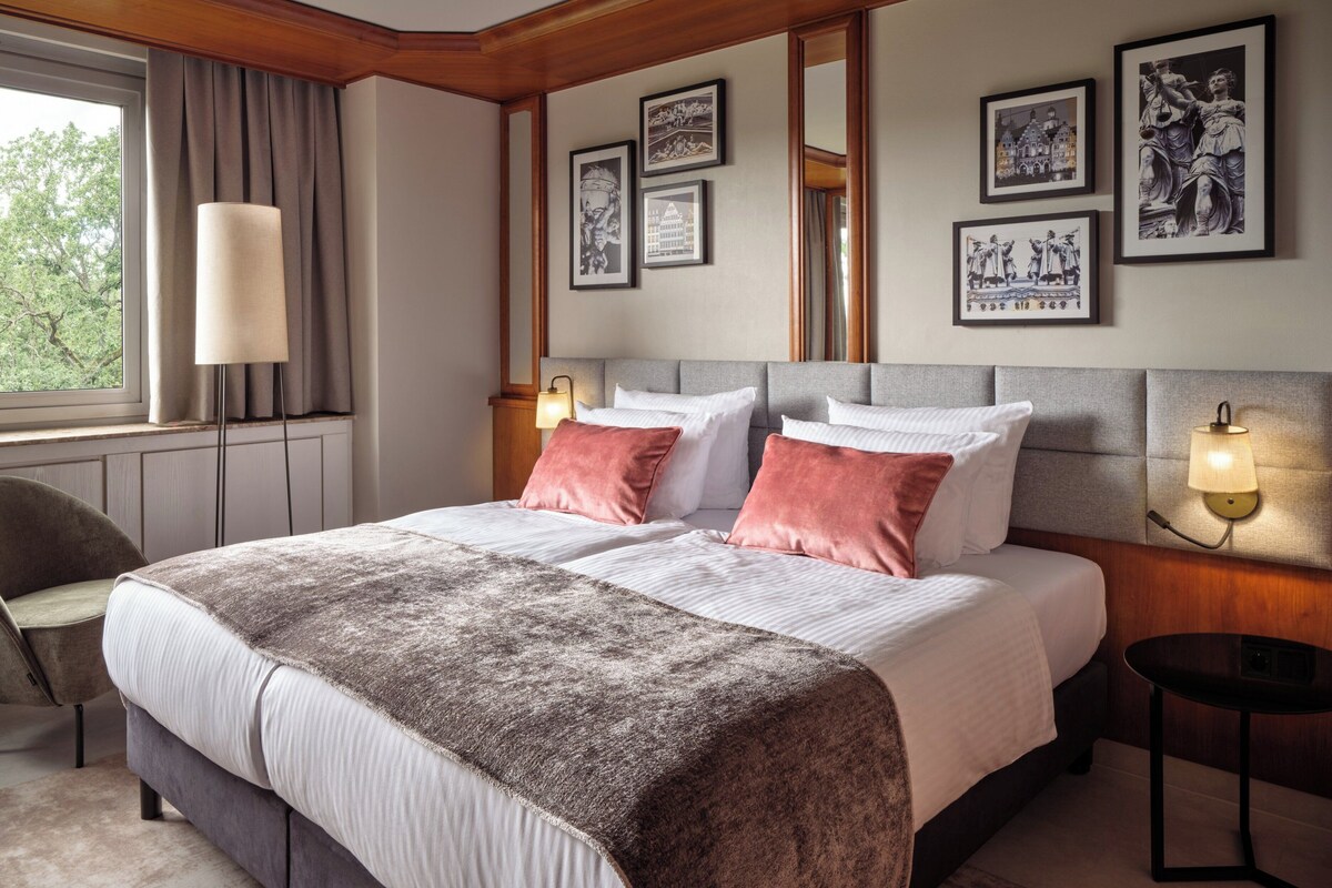 A hotel room with a large bed, a chair, a bedside table, and a lamp.