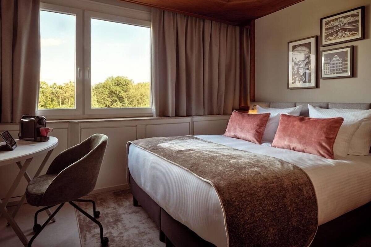 Una habitación de hotel con una cama, una silla, una mesa y un ventanal con cortinas.