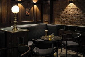 A dimly lit bar area with a wooden wall, a black leather booth, and a round table with chairs. - Leonardo Frankfurt City South (Frankfurt)