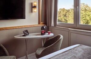 A hotel room with a bed, a small table with a laptop, a coffee maker, and a cup. There is a TV mounted on the wall and a window with curtains. - Leonardo Frankfurt City South (Frankfurt)