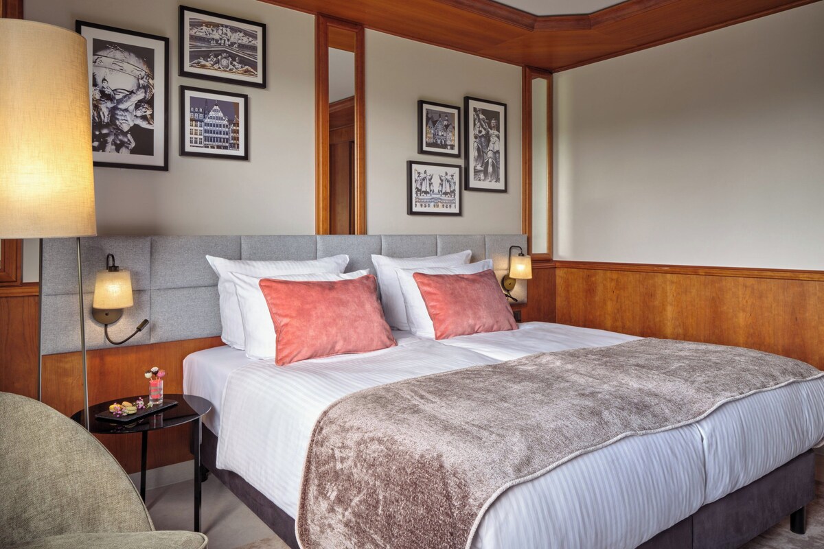 A hotel room with a large bed, two bedside lamps, a small table with a decorative item, and framed pictures on the wall.