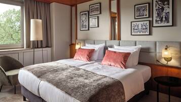 Een hotelkamer met een groot bed, een bureau, een stoel en kunstwerken in lijsten aan de wanden.