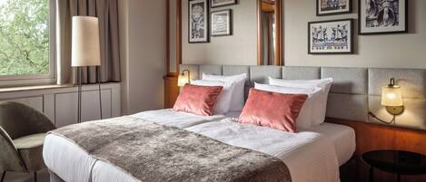 Una habitación de hotel con una cama grande, un escritorio, una silla y cuadros en las paredes.
