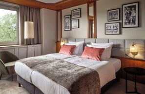 A hotel room with a large bed, a desk, a chair, and framed artwork on the walls. - Leonardo Frankfurt City South (Frankfurt)