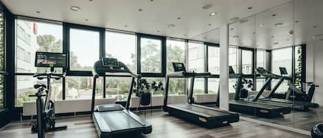 Een moderne sportschool met loopbanden, hometrainers en een spiegelwand.