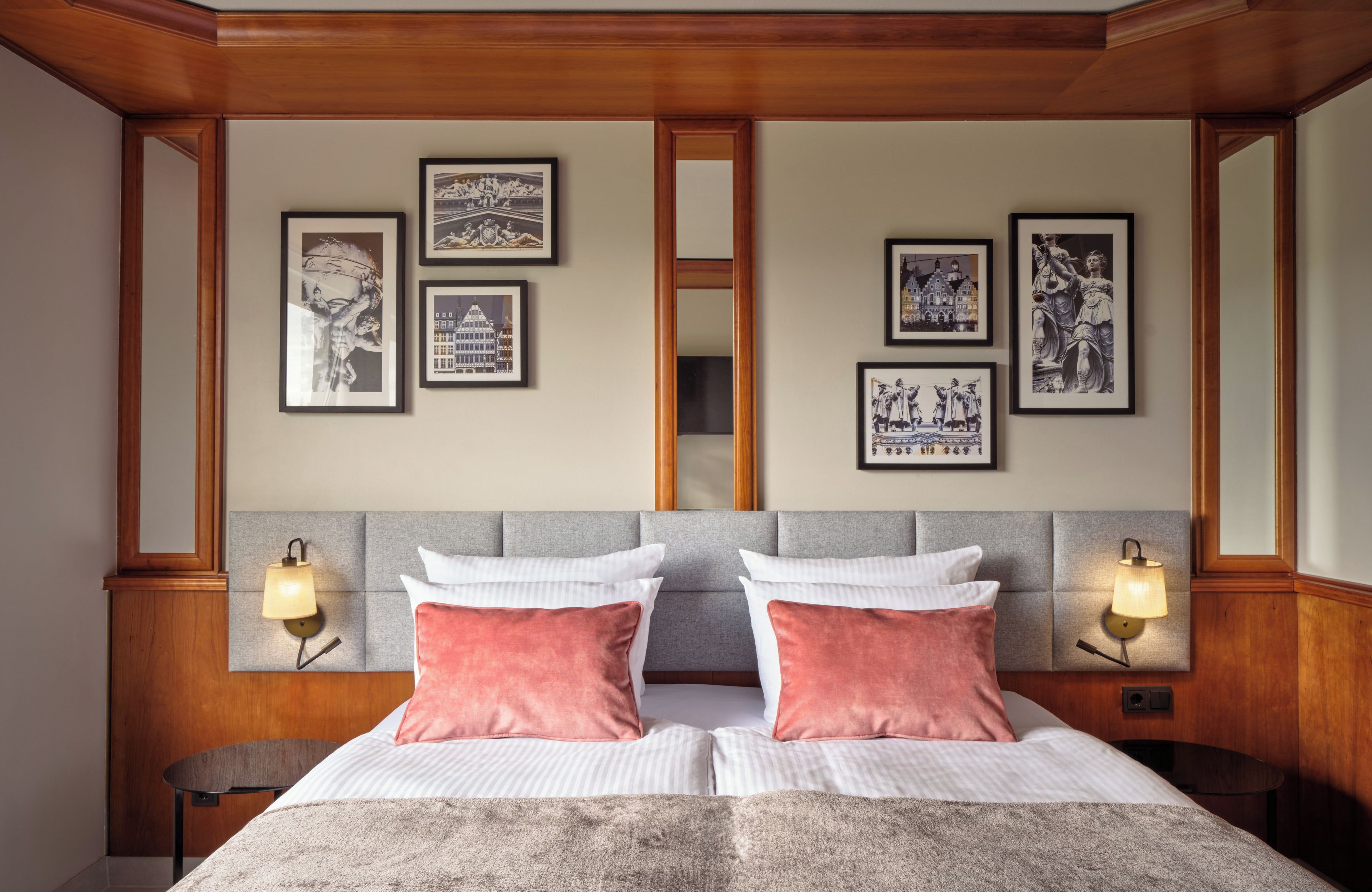 Une chambre d’hôtel avec un grand lit, deux tables de chevet, un miroir et des tableaux encadrés au mur.