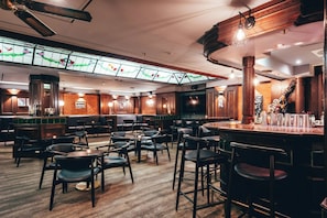 Zona de bar con taburetes de madera, techo alto con vigas a la vista y una ventana de vitral.