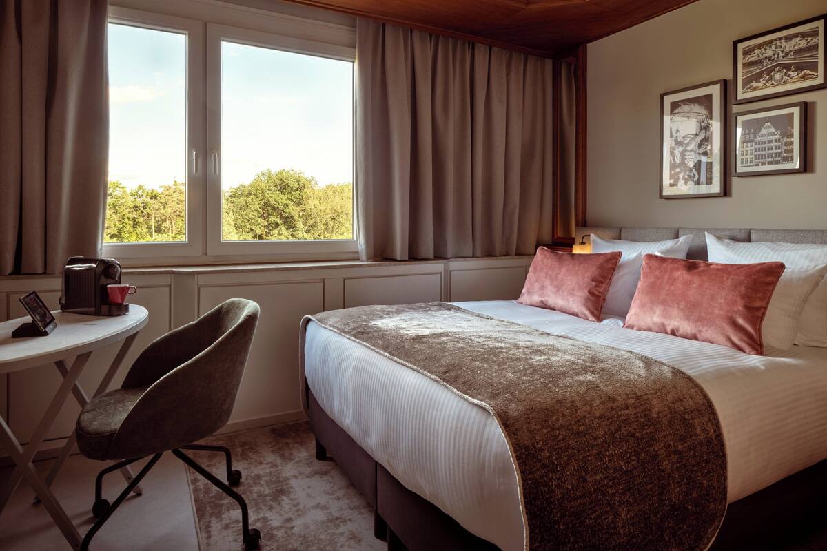 Un dormitorio con una cama, una silla, una mesa y un ventanal con cortinas.