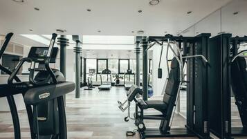 Ett gym med konditionsmaskiner, styrketräningsutrustning och ett stort fönster som släpper in naturligt ljus.