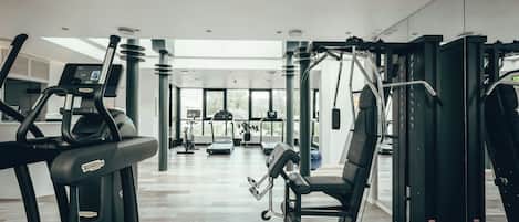 Een fitnessruimte met cardioapparatuur, krachttrainingapparatuur en een groot raam voor natuurlijk licht.