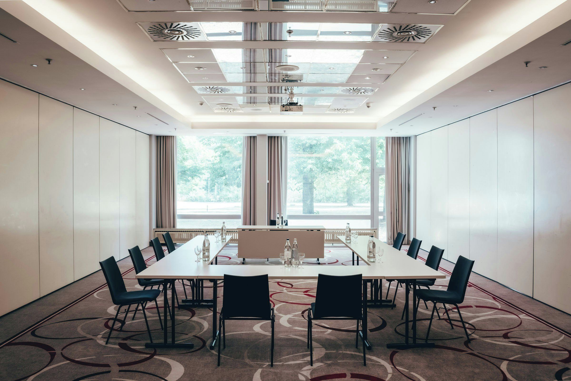 Une salle de conférence avec une longue table, des chaises et une vue sur les arbres à travers de grandes fenêtres.