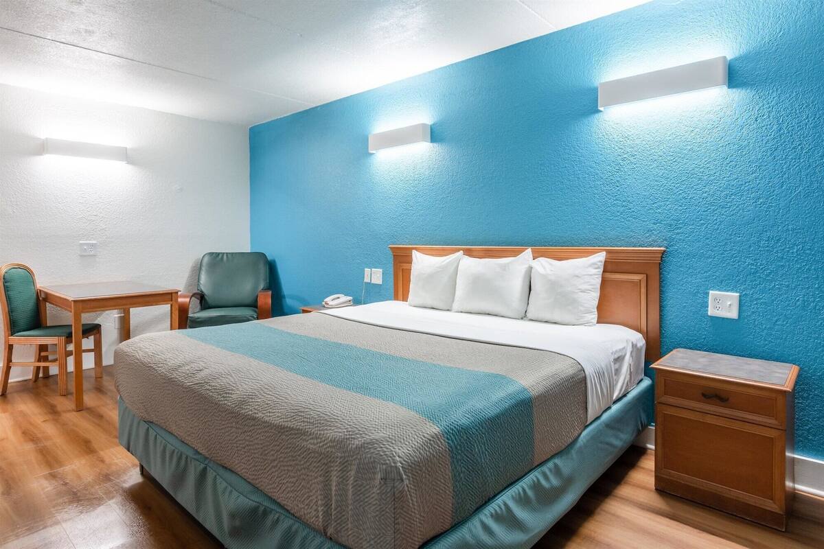 A hotel room with a large bed, a desk, a chair, and a nightstand.