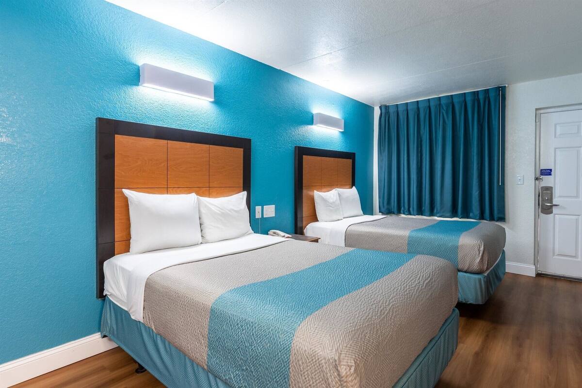 A hotel room with two beds, each with a wooden headboard, white bedding, and a blue and beige patterned blanket.