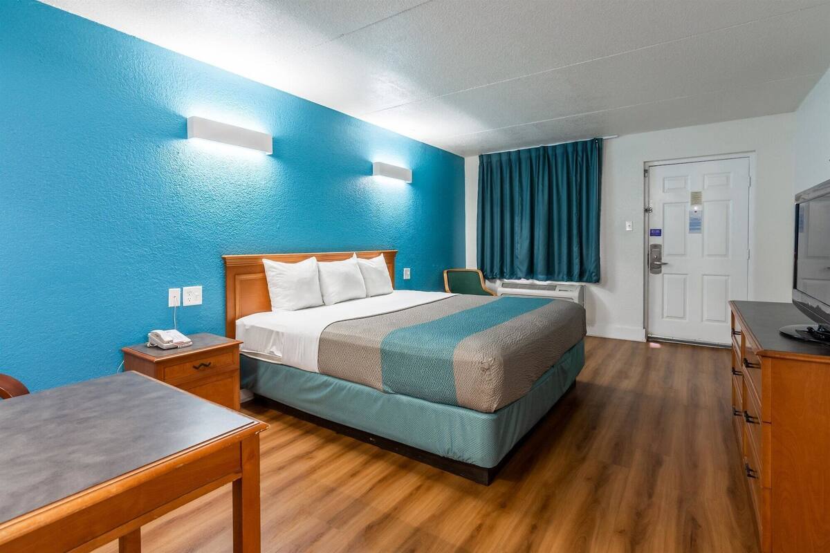 A hotel room with a bed, a desk, a chair, a TV, and a door.