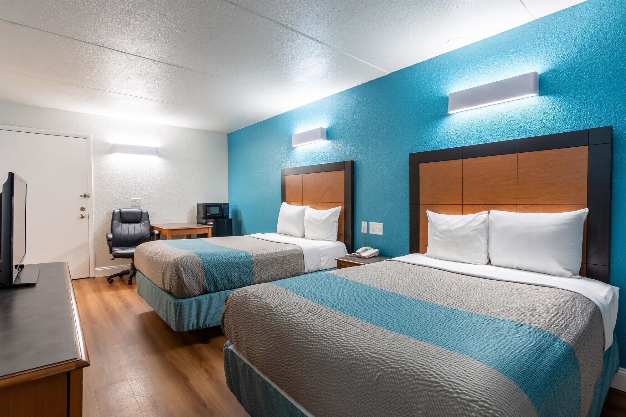 Ett hotellrum med två sängar, ett skrivbord, en stol, en TV och en mikrovågsugn.