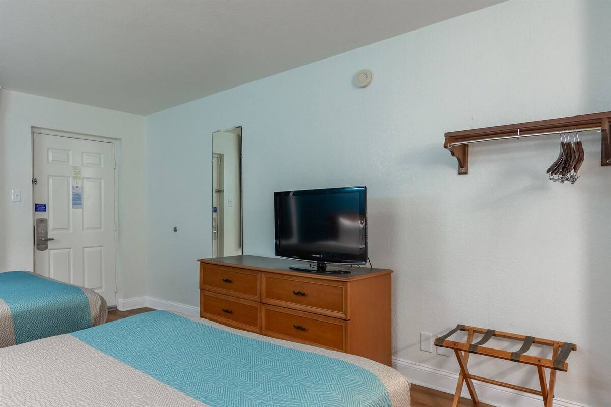A hotel room with a bed, a TV on a wooden dresser, a coat rack, and a door.