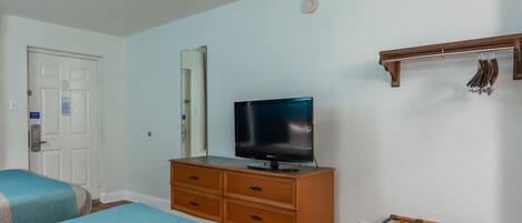Habitación de hotel con cama, televisión sobre una cómoda de madera, perchero y puerta.