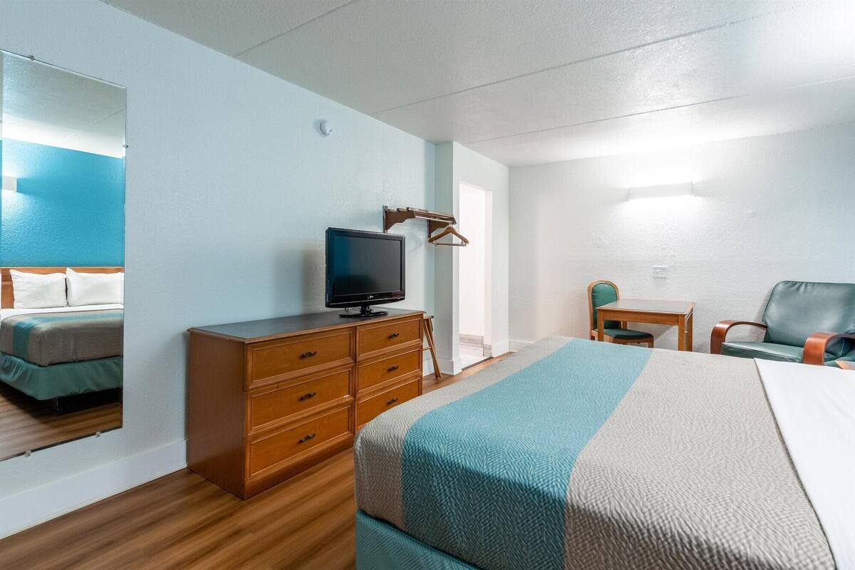 A hotel room with a bed, a dresser, a television, a desk, and a chair.