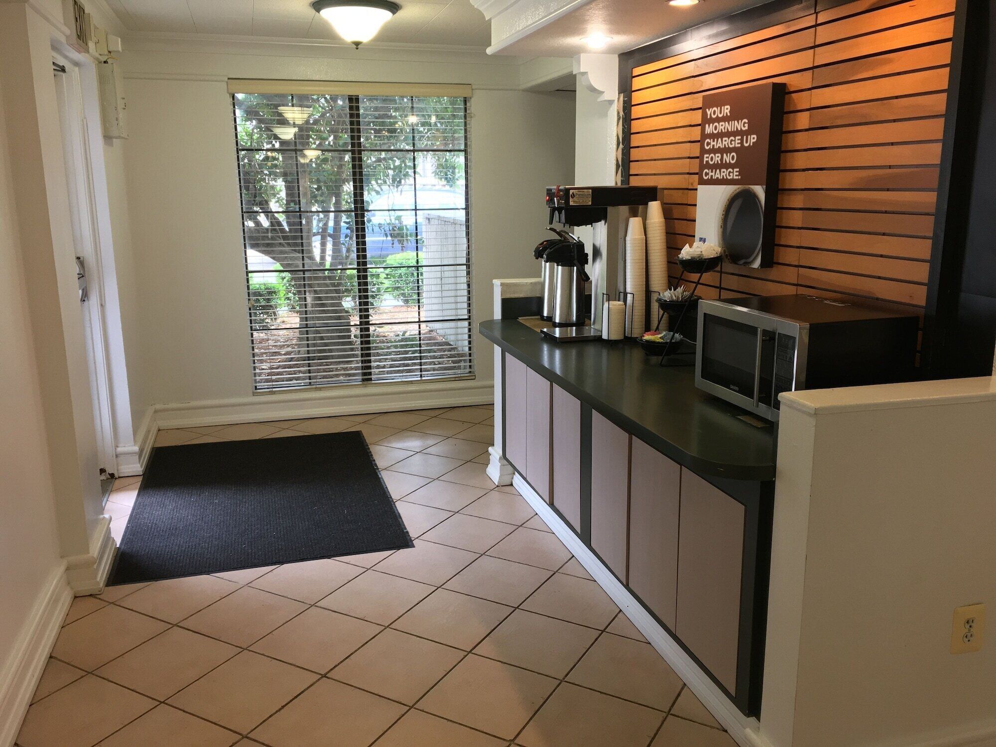 A kitchen with a coffee station, a microwave, and a sign about morning charge-up.