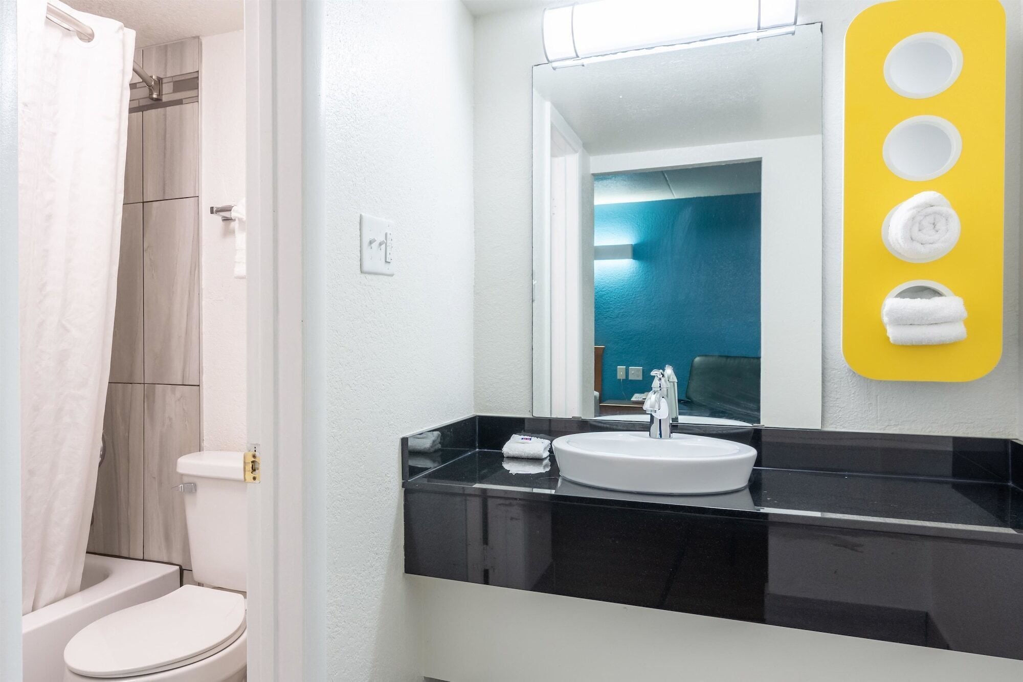 A modern bathroom with a white toilet, a black countertop, and a mirror above the sink.