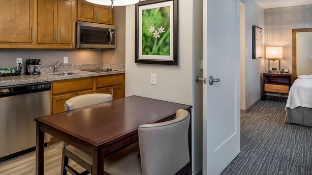 A hotel room with a wooden dining table, a microwave, and a framed picture on the wall. - Homewood Suites by Hilton St. Louis Westport (Maryland Heights)
