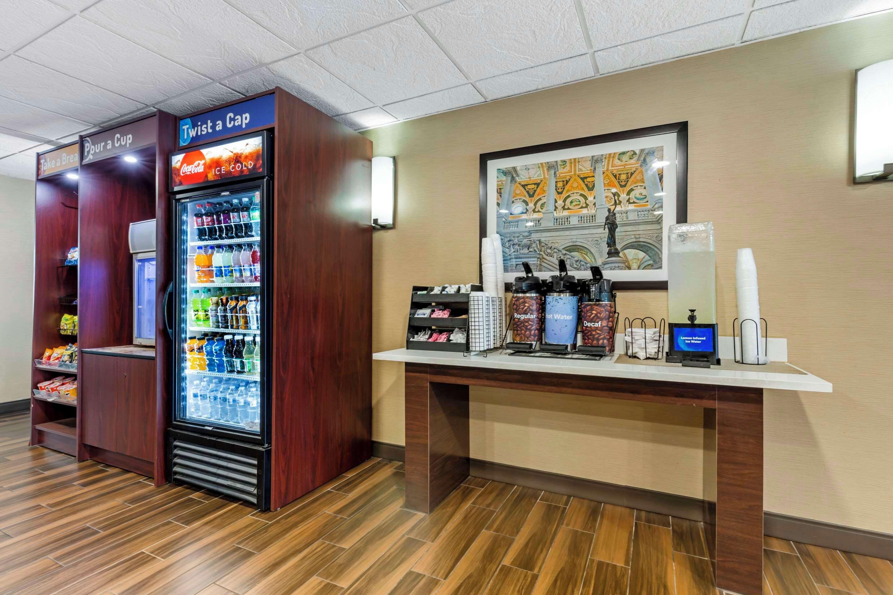 Un espace de libre-service proposant des boissons, avec un réfrigérateur à Coca-Cola et un distributeur de capsules « Twist a Cap ».