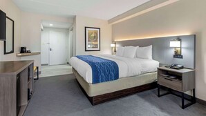 A hotel room with a bed, bedside table, lamp, and a door leading to another room. - Comfort Inn Herndon - Reston (Herndon)