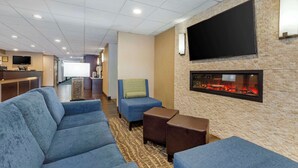 A hotel lobby with a large sofa, a small armchair, a flat-screen TV mounted on a stone wall, and a fireplace. - Comfort Inn Herndon - Reston (Herndon)