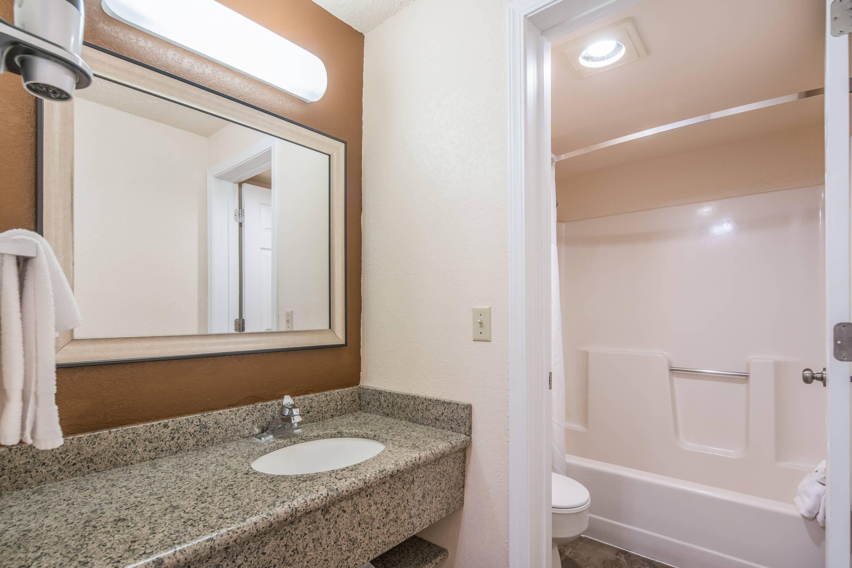 Une salle de bain avec un lavabo à vasque en granit, un miroir, une serviette accrochée au mur et une baignoire blanche.