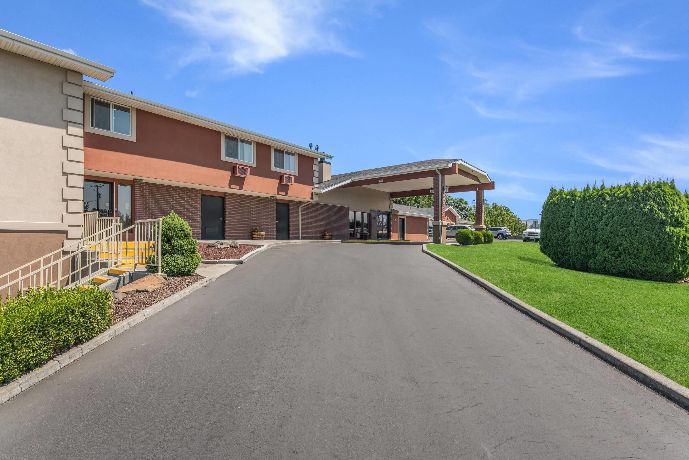 A modern hotel entrance with a covered walkway, a brick facade, and a well-maintained lawn.