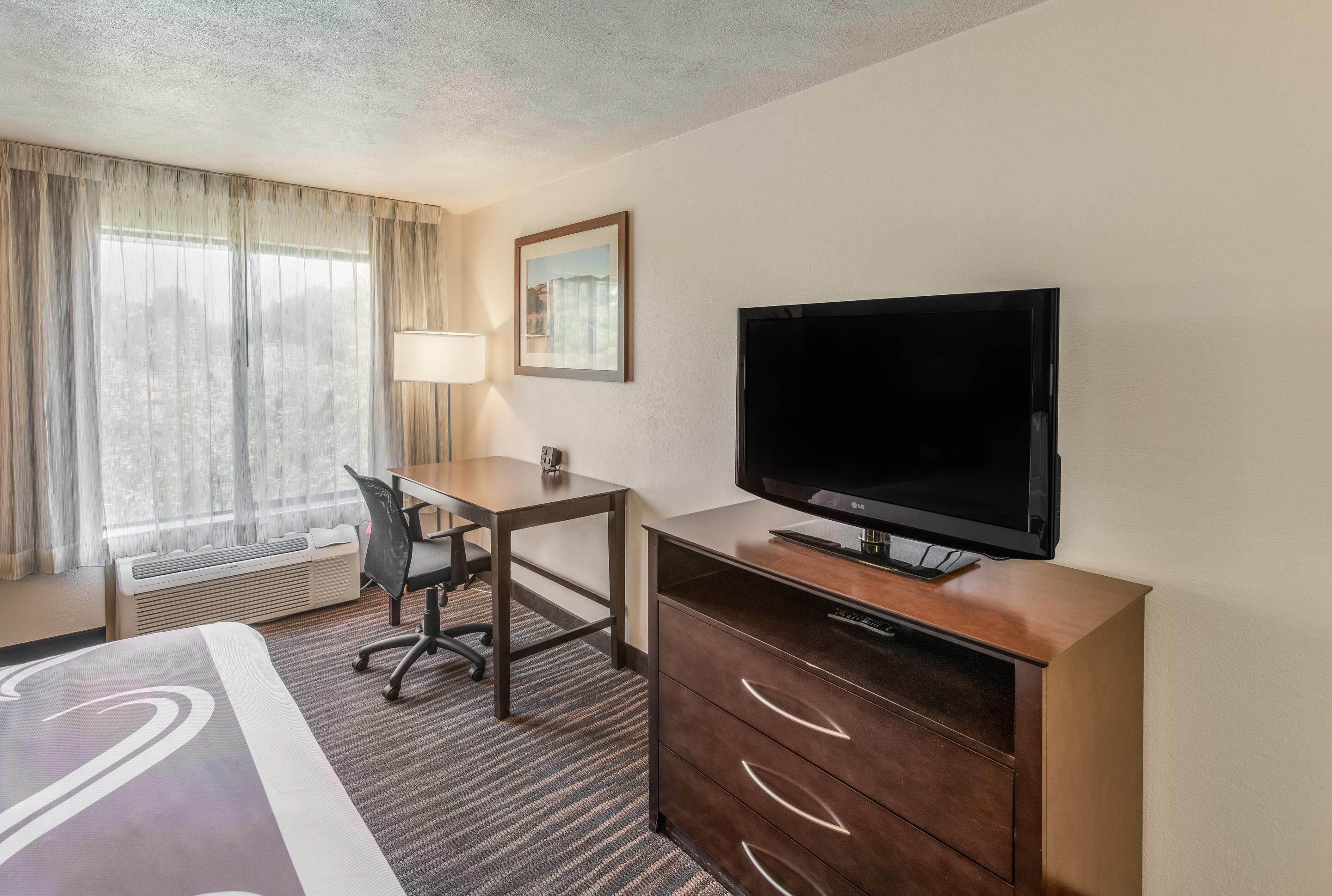 A hotel room with a bed, a desk, a television, and a window with curtains.